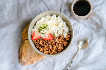 A delicious breakfast bowl with cottage cheese, granola, and strawberries served with black coffee.