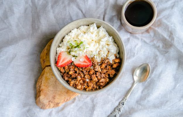 A delicious breakfast bowl with cottage cheese, granola, and strawberries served with black coffee.