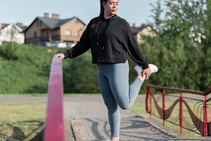Young woman in activewear stretching on a red railing outdoors.